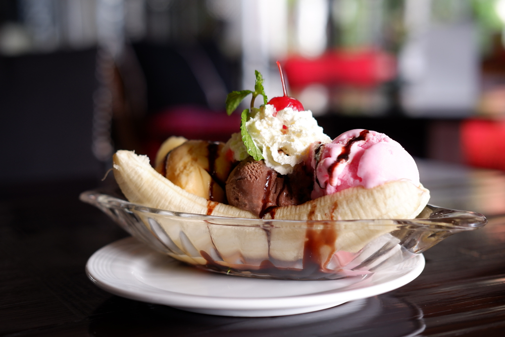 A banana split with vanilla, chocolate, and strawberry ice cream, whipped cream, a cherry, and a sprig of mint. 