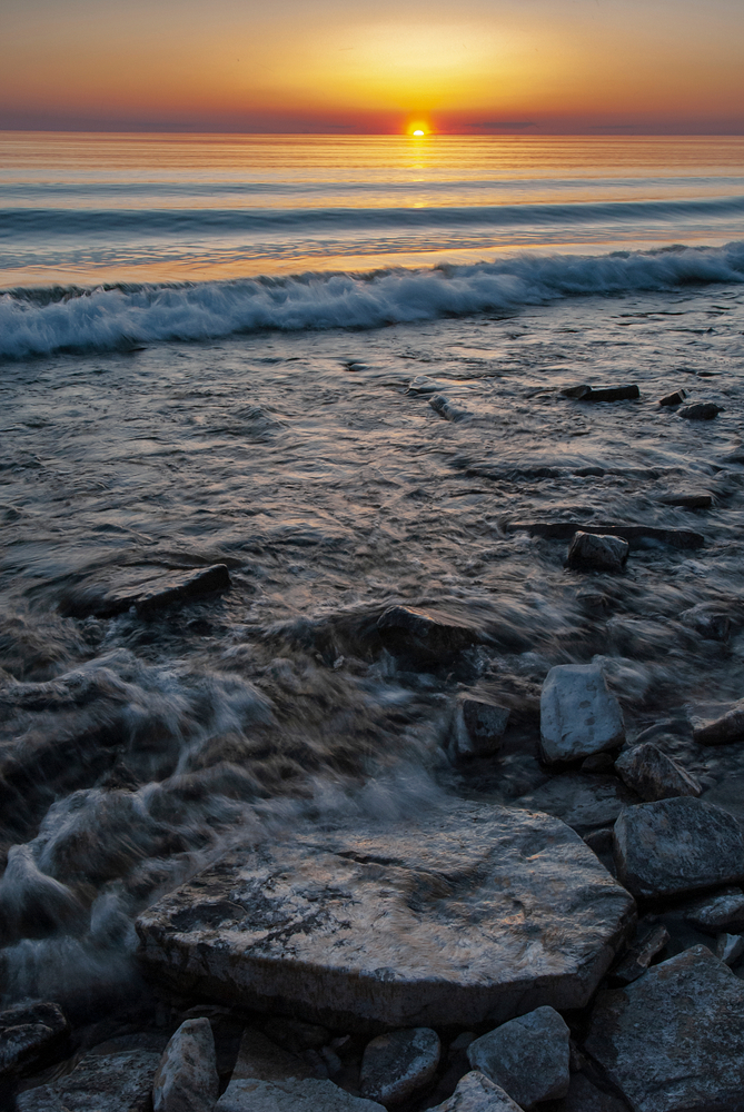 Sunset on Ellison Beach with a wave breaking on the rocky beach 