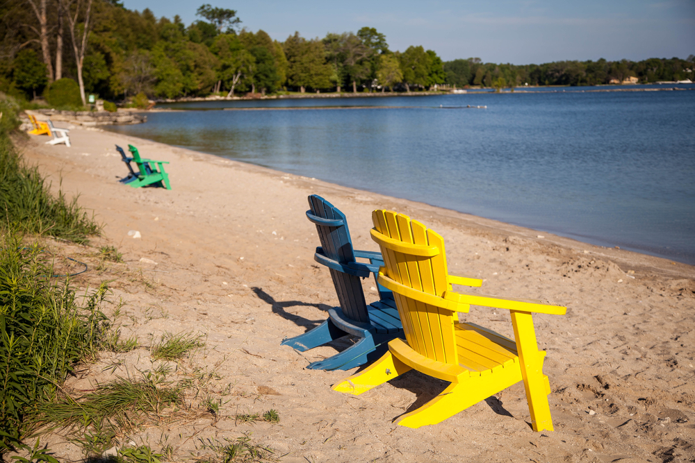 Two comfy Adirondack shairs, one blue and one yellow sitting on sandy Door County WI beach.