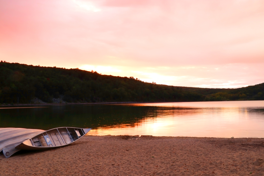 A canoe on the shore of a sandy beach with the lake and hills in the background