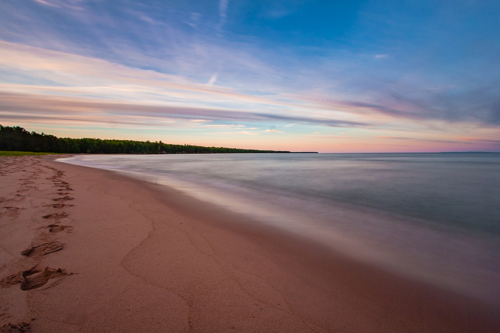 A beautifully calm beach with an expanse of sand and an outcrop of trees