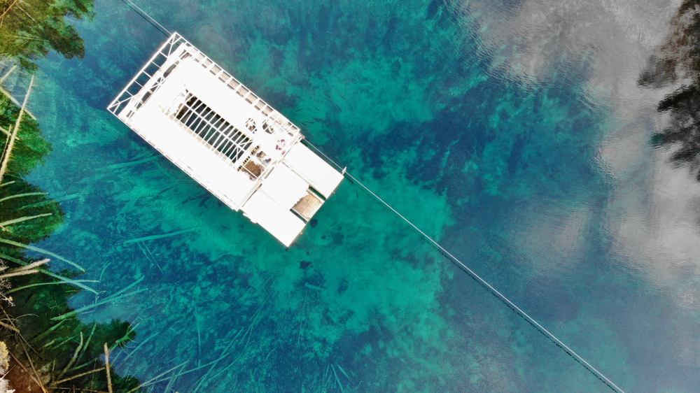 An aerial view of a crystal clear spring in Michigan with a moveable white building floating over it. 