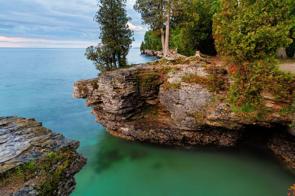 Shoreline showing rocks jutting out into the water with trees around at Cave Point. 