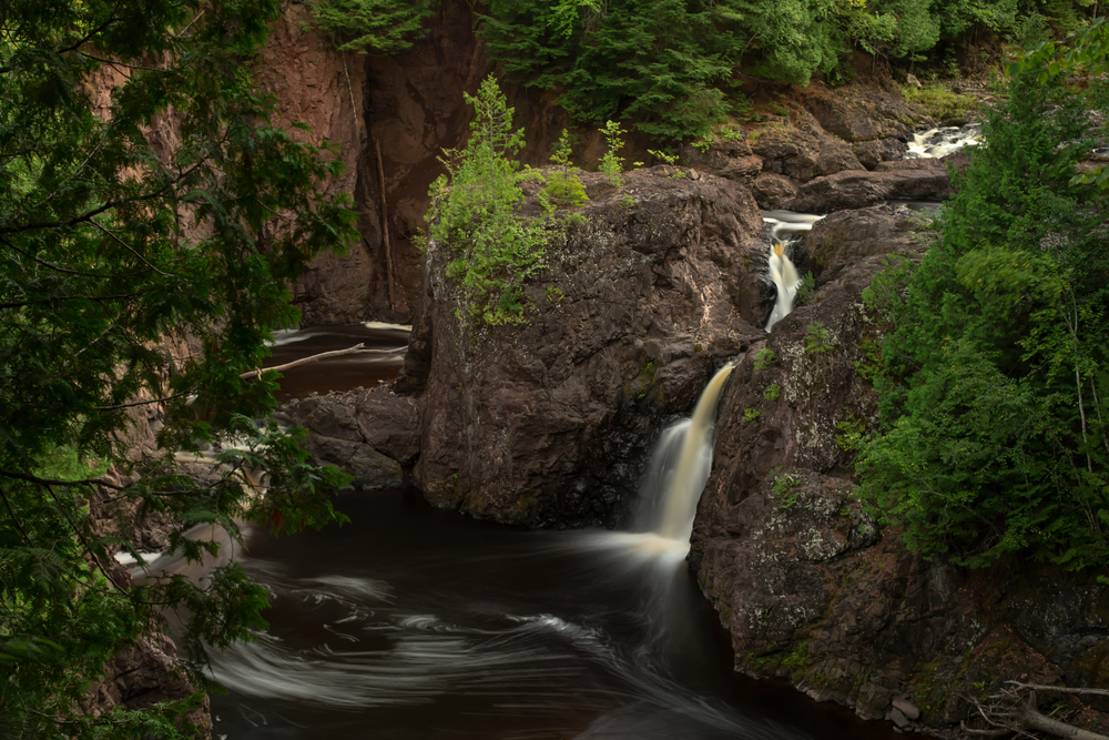 Water tumbling over the rocks into the pool below and folage around. 