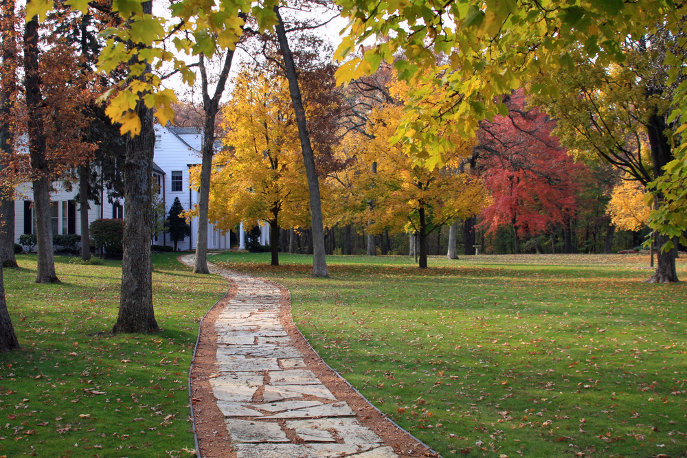 Path leading past a white clapboard house with fall trees all around. 