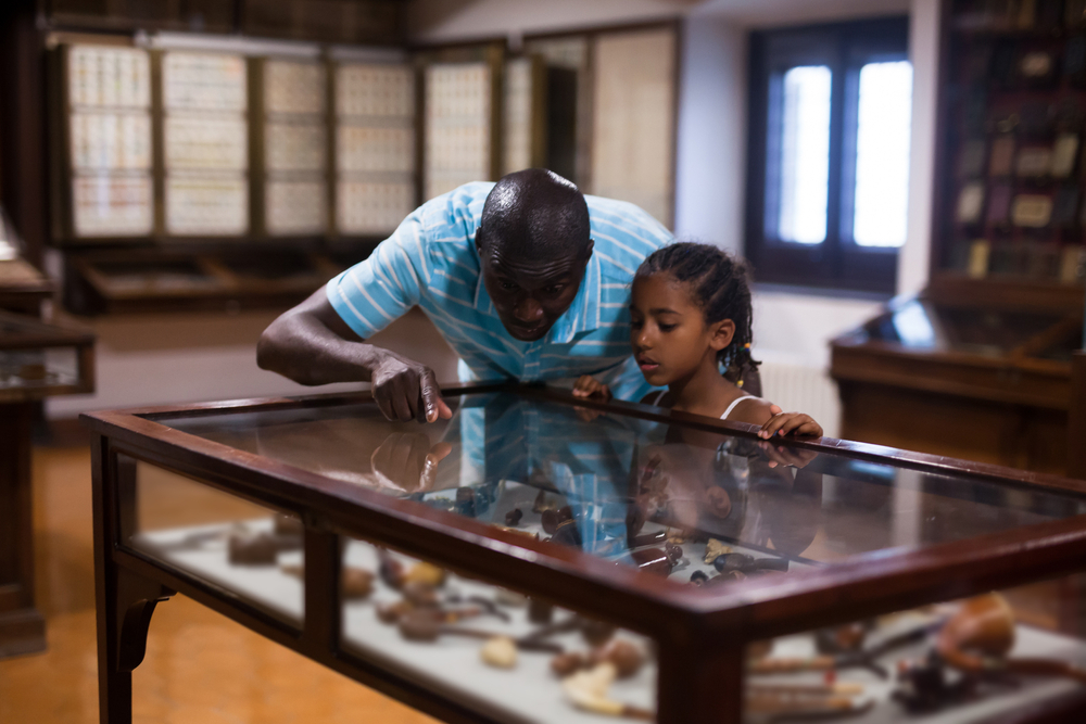 A man and a child looking into a display case at a museum, similar to things you can see at the Kansas African American Museum, one of the best things to do in Wichita.