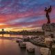 The Keeper of the Plains statue looking over the Arkansas River as the sun sets over Wichita in the distance. It's one of the best things to do in Wichita.