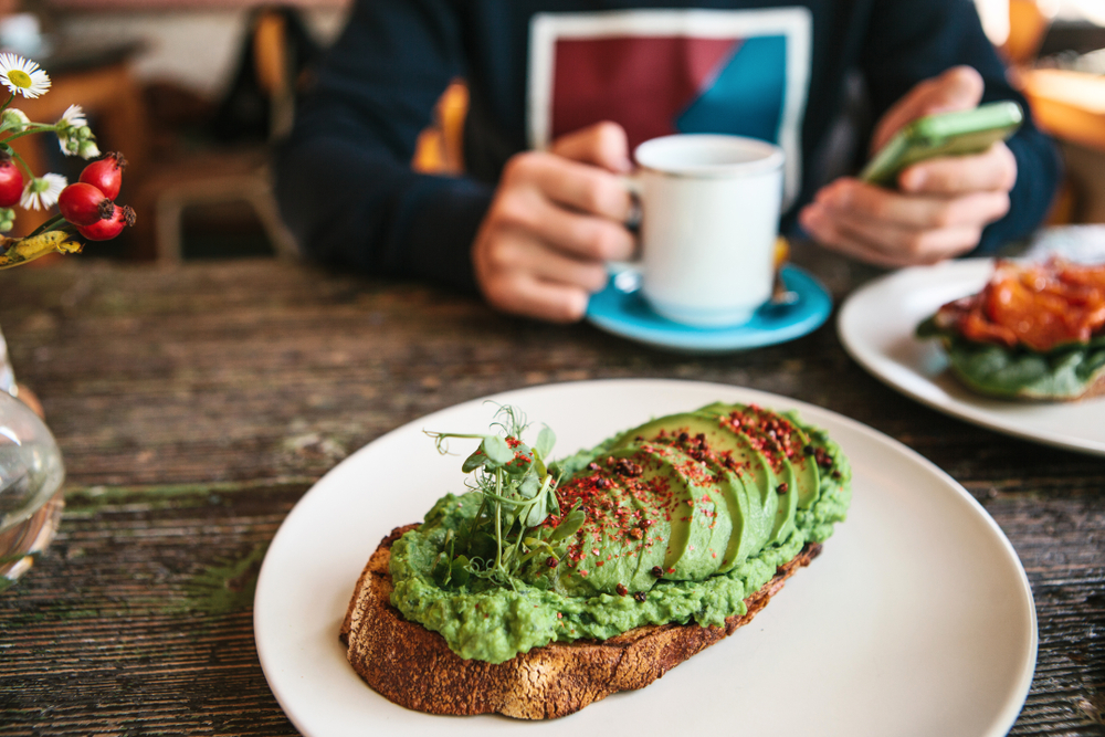 person sitting at cafe table with avacdo toast in front of them. 