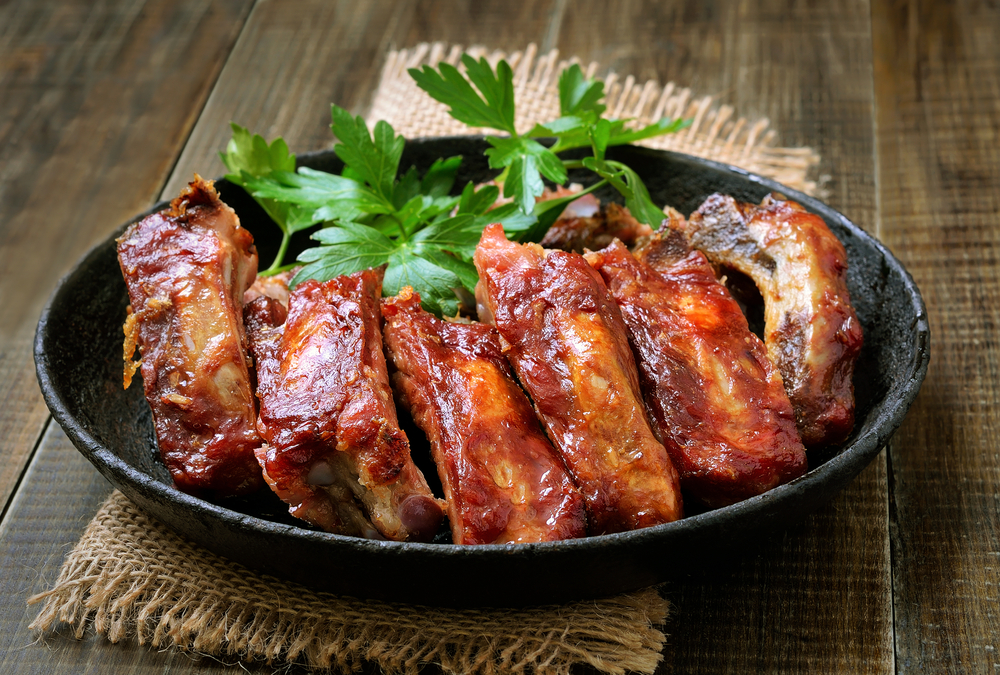 Ribs in a bowl on a table with geen garnish 