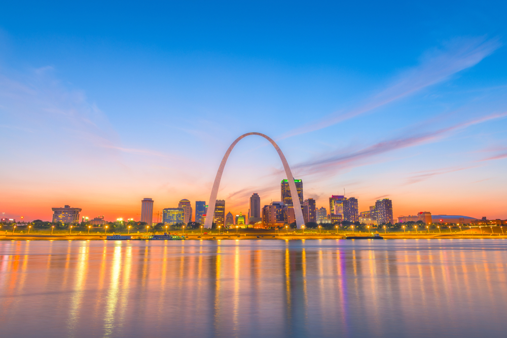 A view of the Gateway Arch and the city of St. Louis from across the river. It is sunrise and the sky is orange and blue. It is one of the best places to visit in the Midwest