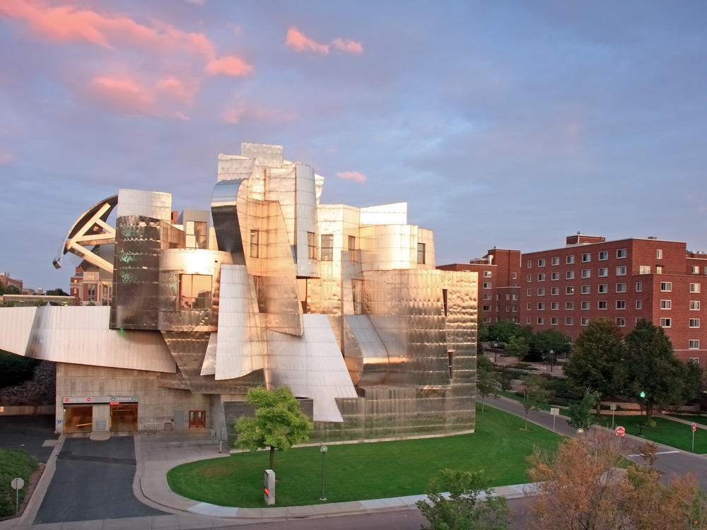 An angular modern aluminum building that is the Weisman Art Museum. The sun is shinning off of it and there is a small green space in front of it. 