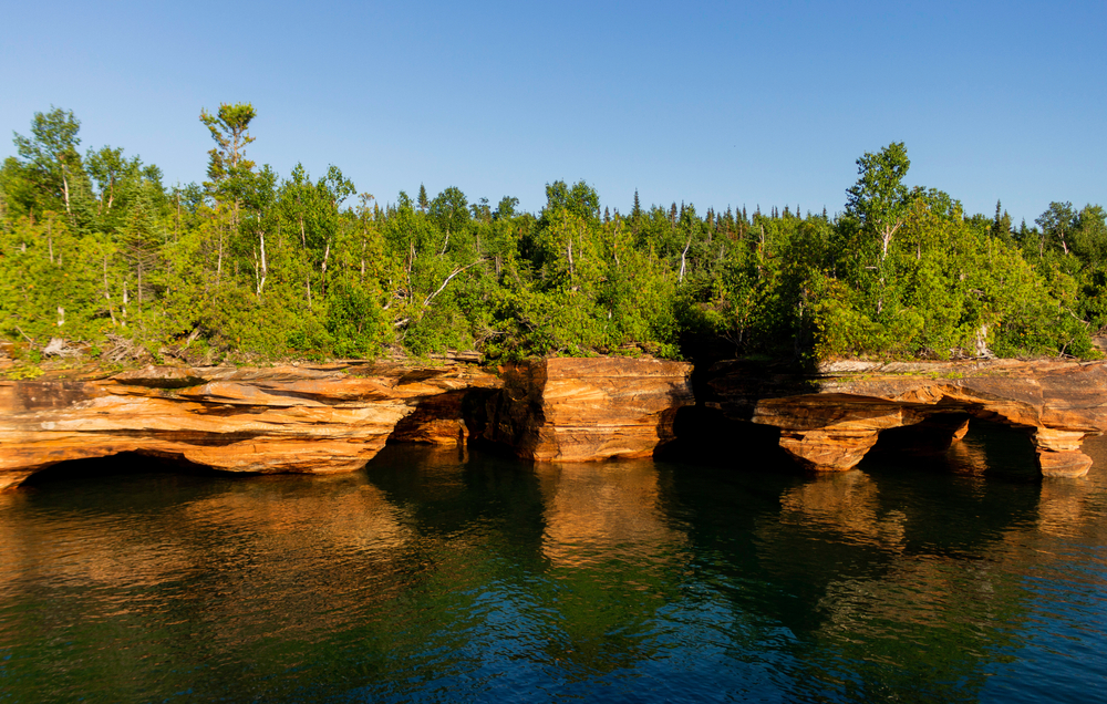 View over the water towards the caves and rocks formations with a forest on top of the islands in the Midwest.