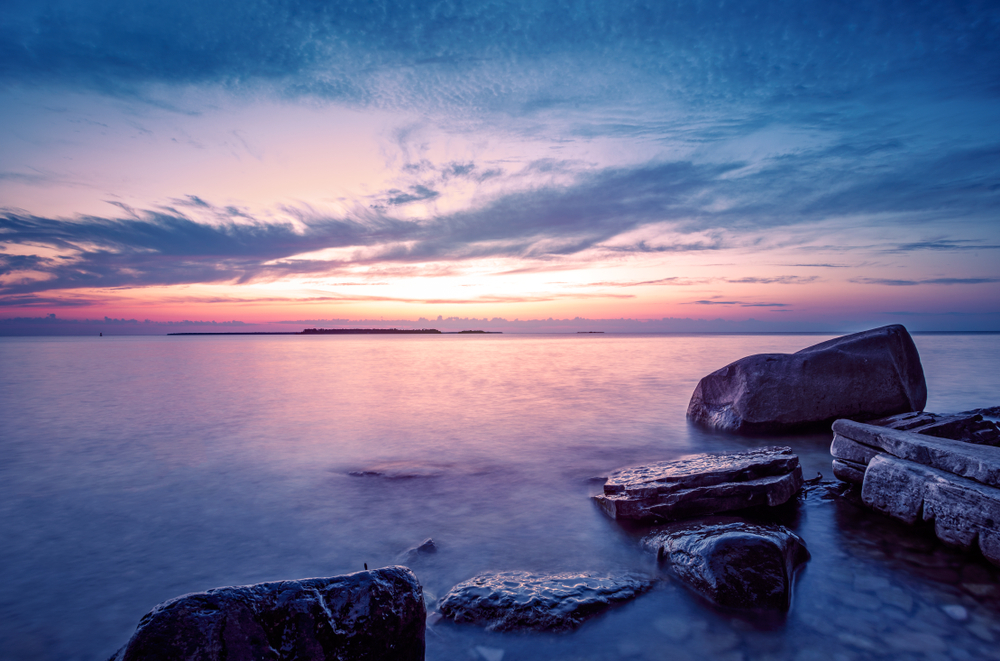 Gorgeous pink and purple sunset over the lake and large rocks in the water.