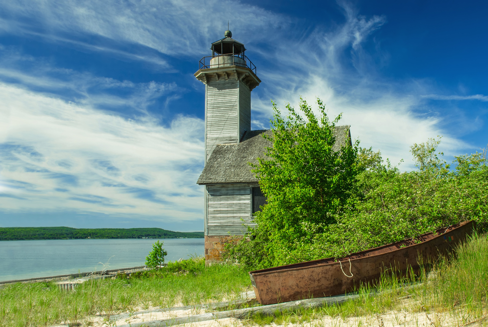 Old, rusted canoe on the shore next to a wooden lighthouse on Grand Island, one of the best islands in the Great Lakes.