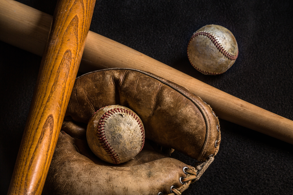 Old, used baseballs, bats, and a glove on a black background.