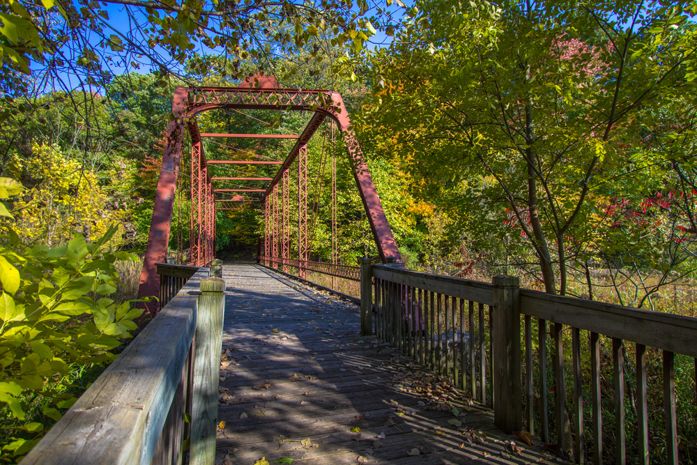 A old, red, metal bridge in a fall-colored forest on a sunny day on one of the best places to hike in the Midwest