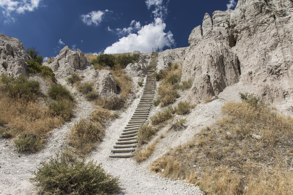  A wooden ladder goes up a sandy desert-like cliff side with blue sky on one of the best hiking trails in Wisconsin.