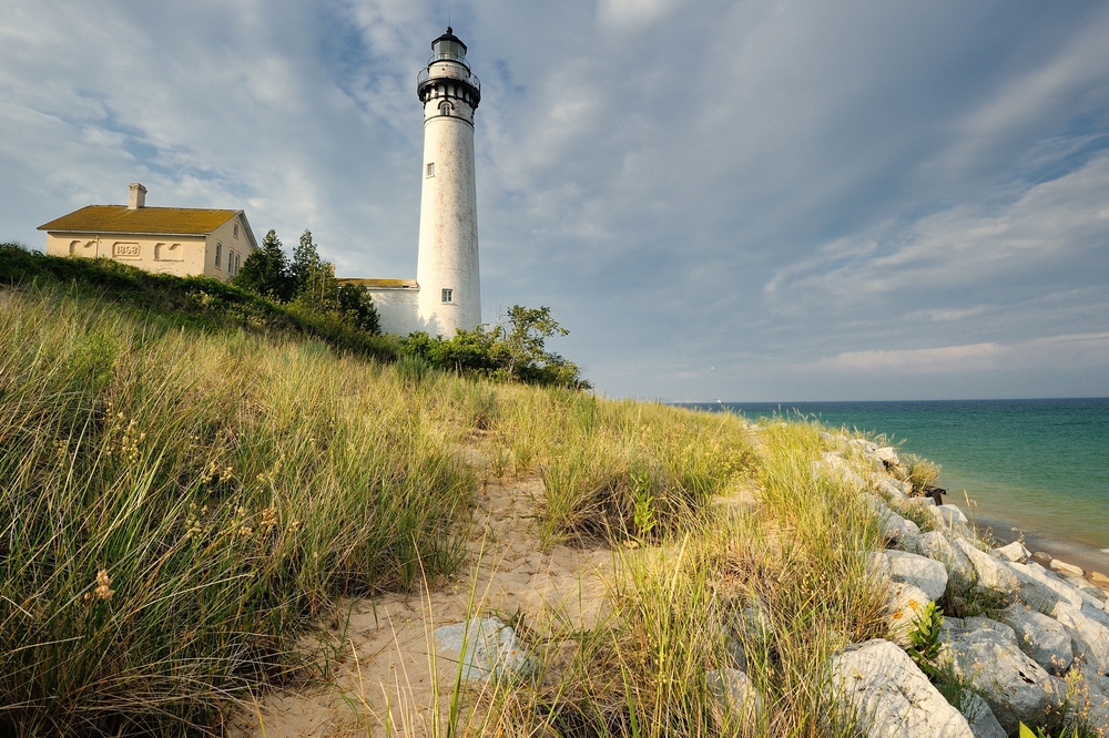 White lighthouse with sandy beach with beach grass and water in foreground form island s in Michigan