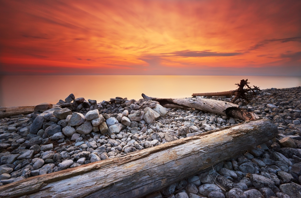 A vivid, orange sunset over the shore of Washington Island with stones and drift wood.