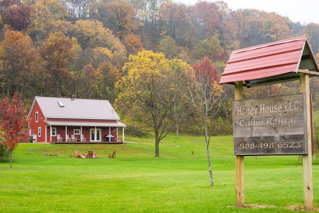 A red log cabin among fall coloured trees and a sign in the forground. 