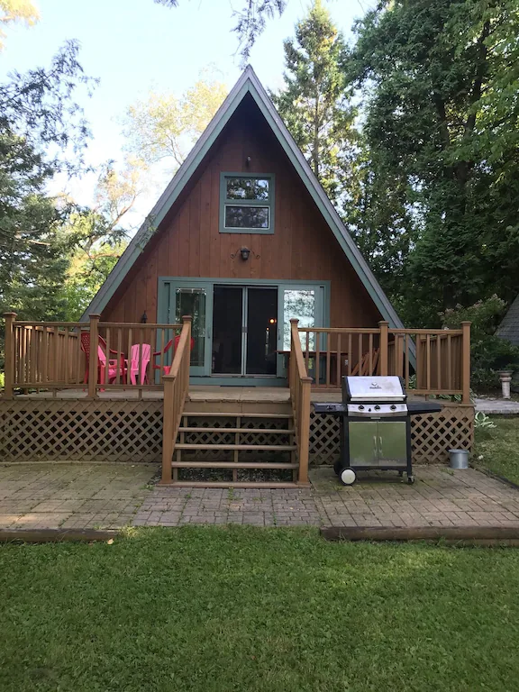 A frame cabin with a large deck. Chairs are on the deck and there is a grill on the patio below.  One of the cabins in Wisconsin to look into.