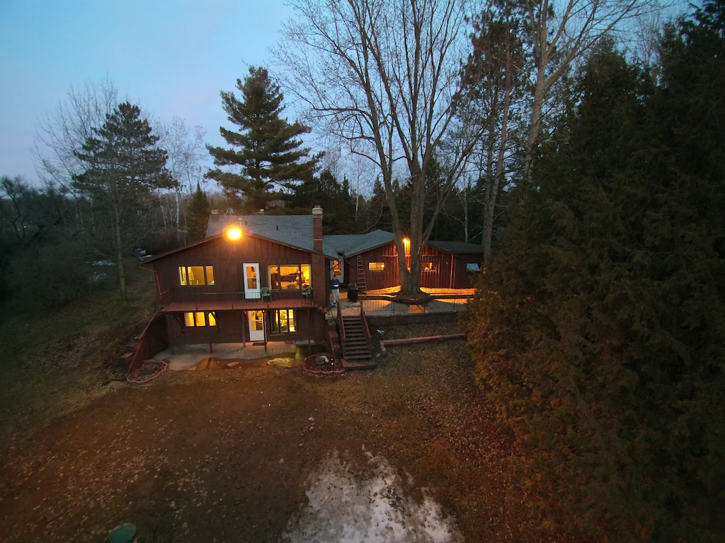 A large cabin in a clearing with the lights on at nighttime