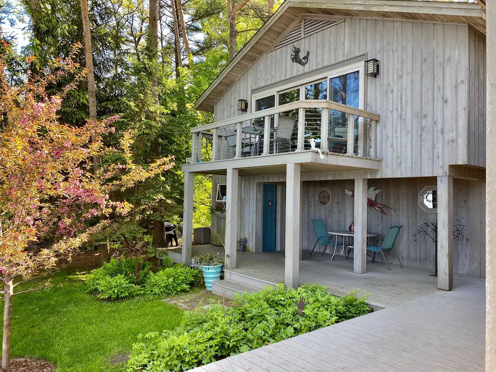 Grey cabin with a large balcony in a spring garden in an article about cabins in Wisconsin