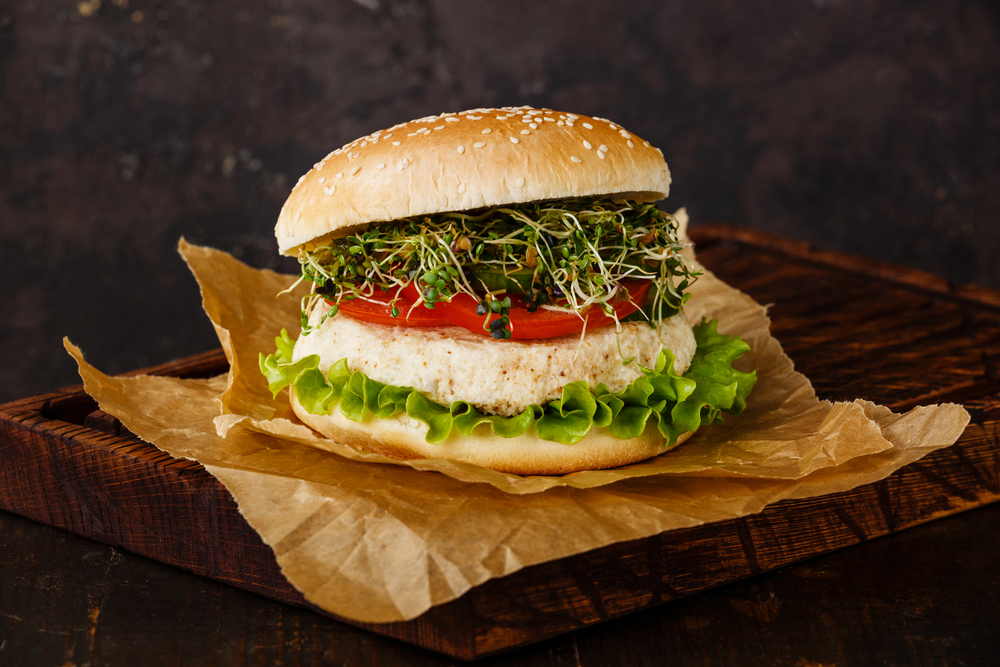 A cauliflower burger with bean sprouts, tomato, and lettuce on top of it. Its similar to burgers you can find at restaurants in Topeka.