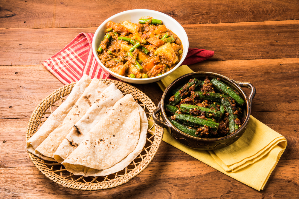 A plate of Indian flat bread, a dish with potatoes, curry, and peas, and a bowl of okra with spices. Served at a great Topeka KS restaurant.