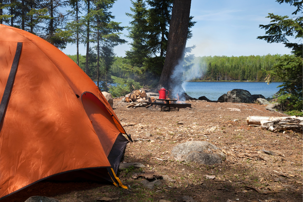 The side of an orange tent next to a lake. You can see a red kettle being warmed up on a fire. Similar to one of the best places for camping in Minnesota.