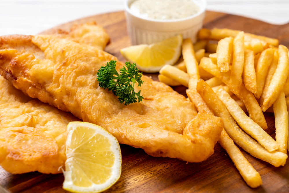 Freid fish and chips on a board with a spring of parsley and a side of tartar sauce. 