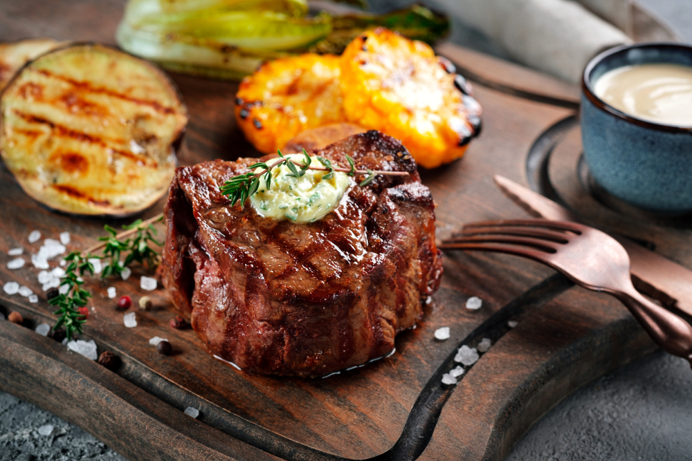 A fillet steak on a wooden board and sweetcorn and aubergine slices. 