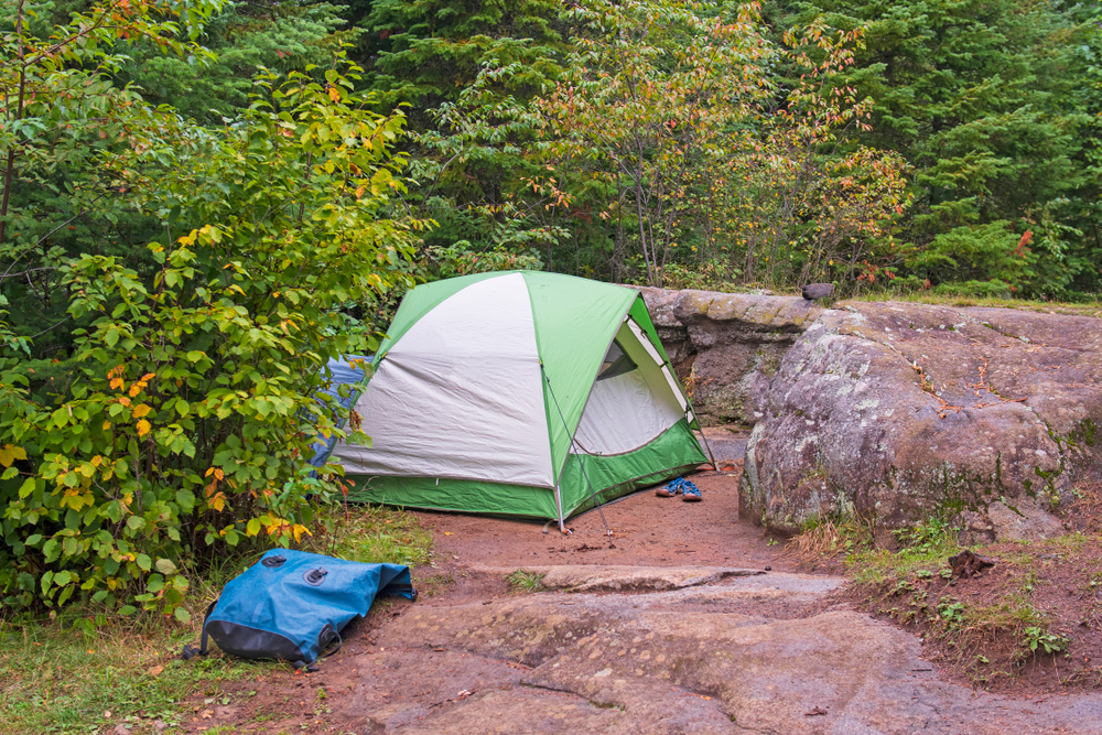 A green and grey tent near a rock formation in a secluded campsite. Its similar to places to go camping in Minnesota. 