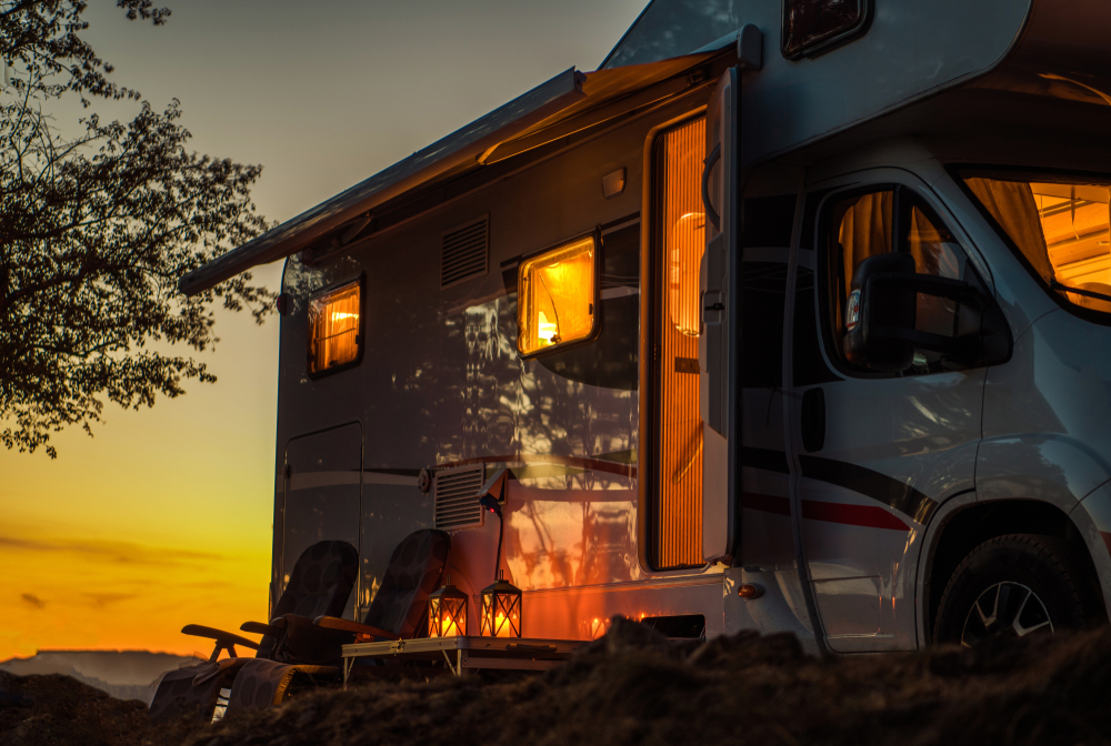 The side of an RV as the sun is setting. You can see light coming from inside the RV and the sun setting in the distance. Camping in Minnesota.