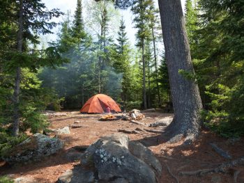 An orange tent in a secluded campsite surrounded by boulders and trees. It's similar to some of the best places for camping in Minnesota.