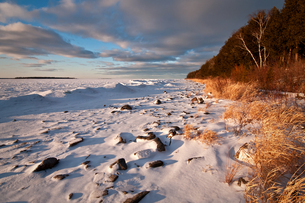 A snowy outlook with trees off to the right and stone peeking through the snow at one of the best state parks in Wisconsin. 