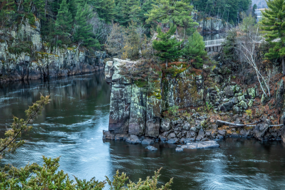 A river surrounded by high cliffs  with trees on the cliffs and a bridge in the background at one of the best state parks in Wisconsin.