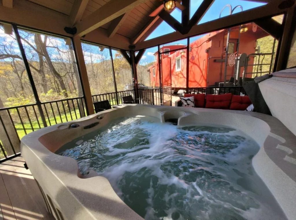 The view of a private hot tub in a screened in porch. Next to the porch you can see a bright red antique railroad caboose. 