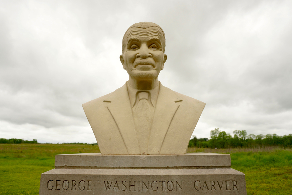 Close up of a bust of George Washington Carver with a field in the background on a cloudy day.