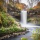 Waterfalls cascading over rocks into pool of water below surrounded by autumnal colored trees while hiking in Minnesota