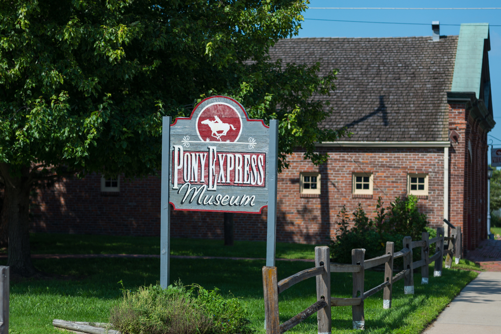 Wooden sign of the Pony Express Museum outside of the brick building.