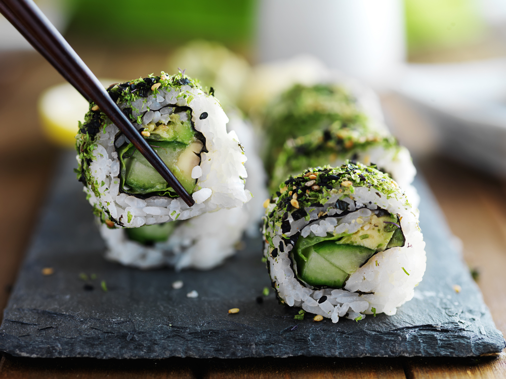 avocado and kale sushi rolls with chopsticks on a black plate