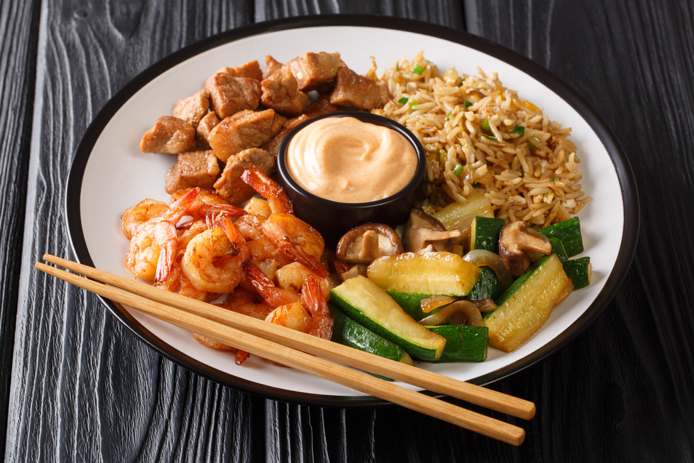 a white place with hibachi of rice, shrimp, steak and vegetables served along with chopsticks