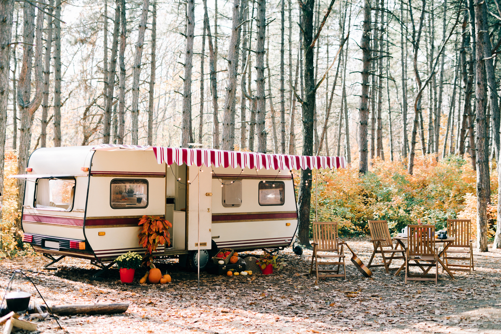 A cute camper with a red and white awning and a set of tables and chairs outside surrounded by woods. One of the best places for camping in Missouri. 