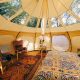 Inside a lotus belle tent that has the ceiling screens open so you can see the treetops. It has a bed and two chairs with very colorful patterned fabric in it. It's one of the best options for glamping in Wisconsin.
