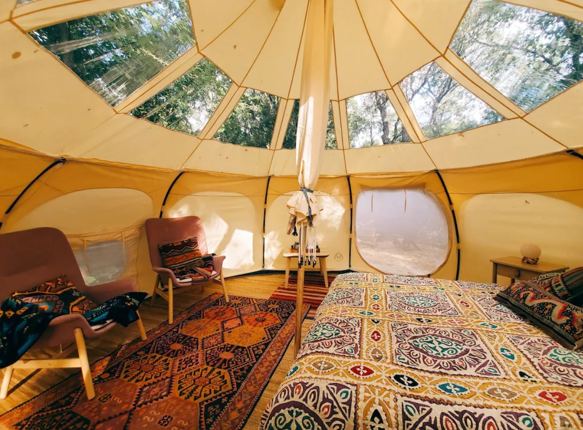 Inside a lotus belle tent that has the ceiling screens open so you can see the treetops. It has a bed and two chairs with very colorful patterned fabric in it. It's one of the best options for glamping in Wisconsin.