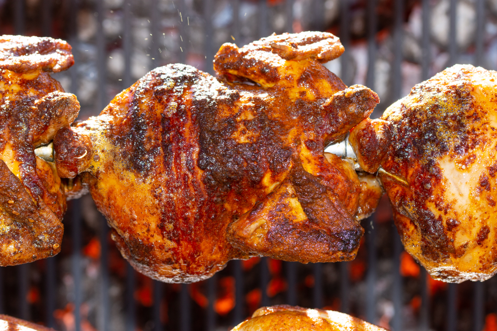 Rotisserie ,Roasted chickens on spit grilled over fire of a big barbecue. In an article about restaurnats in Lake Geneva. 