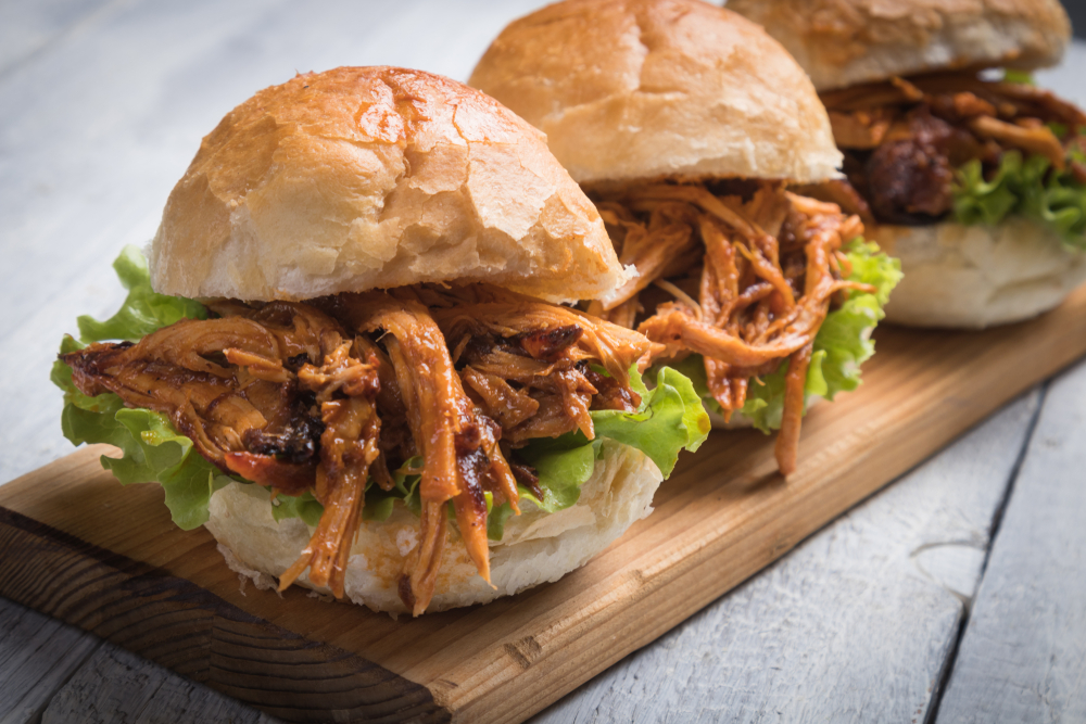 Three pork sliders on a wooden tray. Pulled pork and lettuce in a bun in an article about restaurants in Oshkosh. 