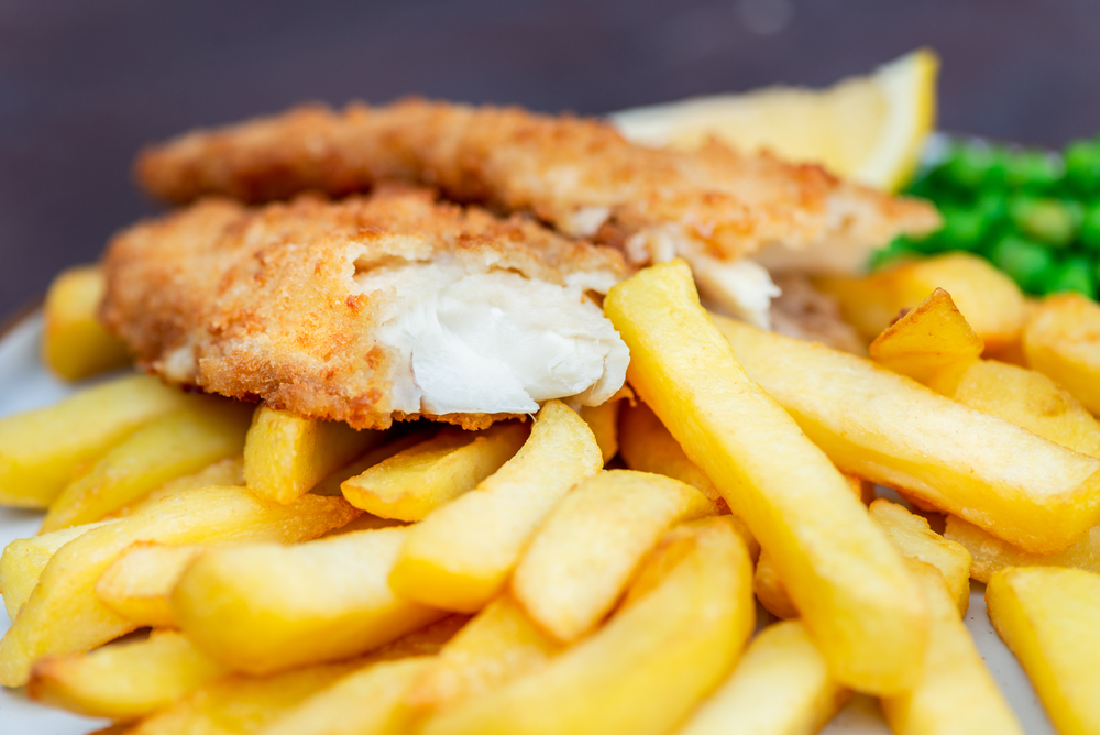 Close up of a plate of fish and chips with peas. The fish is cut in half showing the white fish inside the batter.  