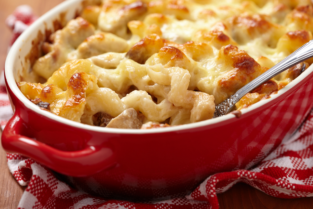 A dish of backed mac and cheese in a red serving dish with a spoon in.  The dish is sitting on a red and white checked napkin.  